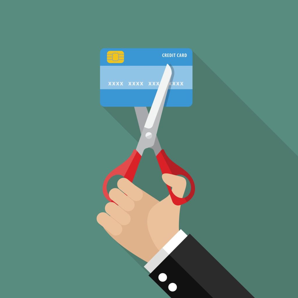 A man cutting a credit card with scissors on a green background while demonstrating how to pay off credit card debt fast.