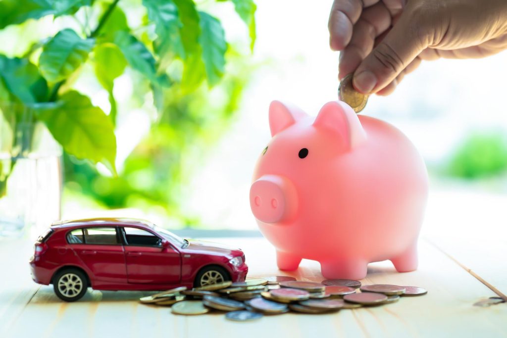 A person is putting coins into a piggy bank next to a car. They are saving up for a $1000 down payment on a car with no credit check.